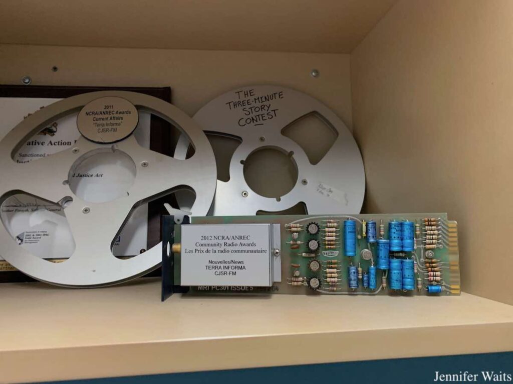 Photo of awards at campus and community radio station CJSR. Pictured are two silver tape reels, one of which has "2011 NCRA/ANREC Awards Current Affairs 'Terra Informa' CJSR-FM" written on it. The other reel is labeled "The Three-Minute Story Contest." And in the foreground, a circuit board has a label on it that reads "2012 NCRA/ANREC Community Radio Awards Les Prix de la radio communautaire Nouvelles/News Terra Informa CJSR-FM." Photo: J. Waits