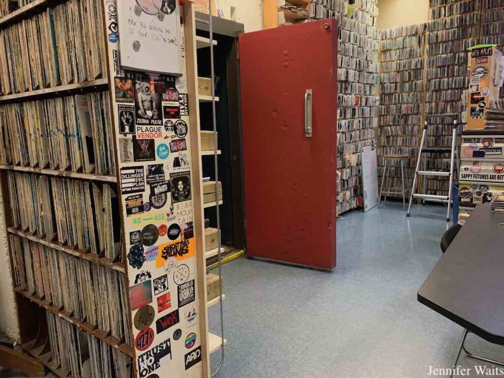 Photo of campus and community radio station CJSR. To the left are shelves of vinyl records. At the center is an open heavy red door, which leads to the on-air studio. To the right are shelves full of CDs. Photo: J. Waits