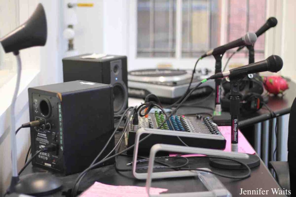 College radio station WPIR Pratt Radio studio in March, 2023. In the photo: 3 microphones on stands, a mixing board, two monitor speakers, a turntable, a lamp, and headphones. Photo: J. Waits