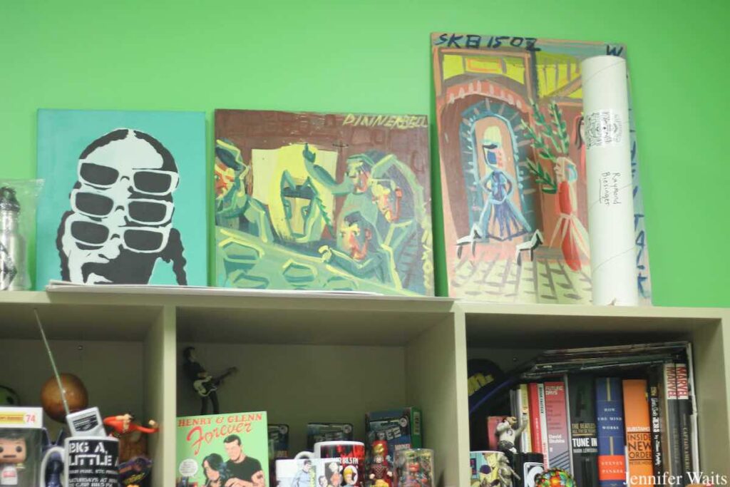 Photo of office at CJSR-FM. There's a bright green wall and a shelf with colorful paintings perched on top and books, toys, mugs, and figurines on the lower shelf. Photo: J. Waits