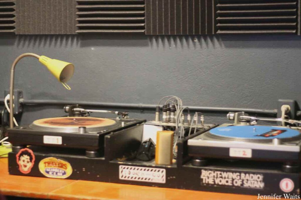 Photo of two turntables in studio of campus and community radio station CJSR-FM. Stickers are affixed below the turntables, including one for record label Touch and Go and another that reads "right-wing radio the voice of Satan." Photo: J. Waits