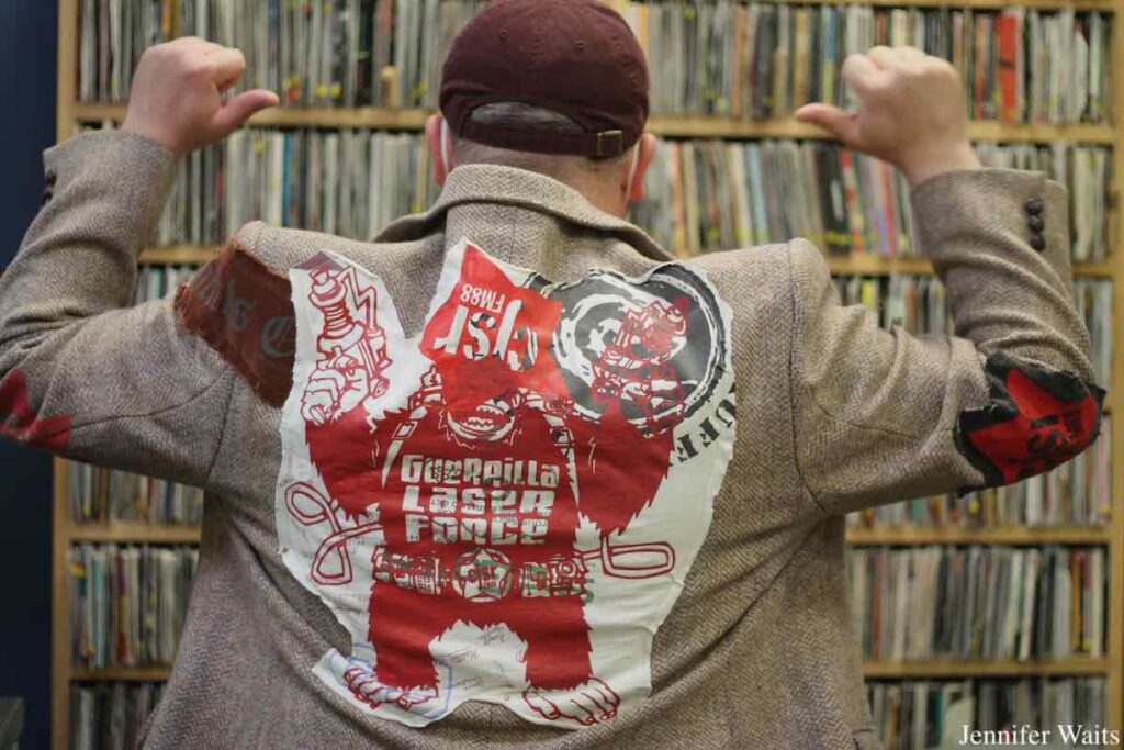 Photo of man wearing a sport coat that has been decorated with patches promoting campus and community radio station CJSR. The back of the jacket has an illustration of a gorilla and reads "Guerrilla Laser Force." Photo: J. Waits