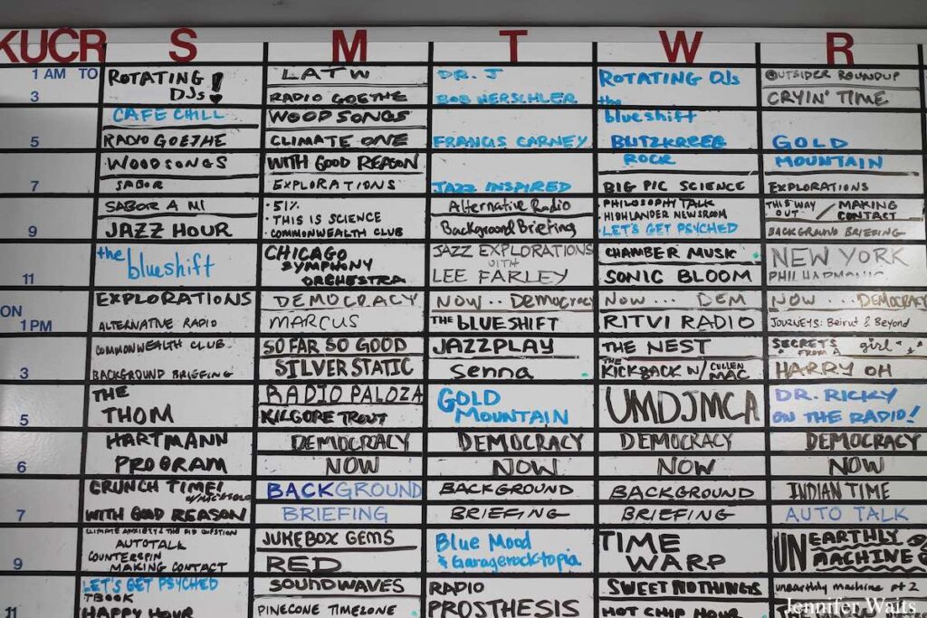 Photo of dry erase board with handwritten weekly schedule for college radio station KUCR. Show names are written in squares for each time slot. Photo: J. Waits